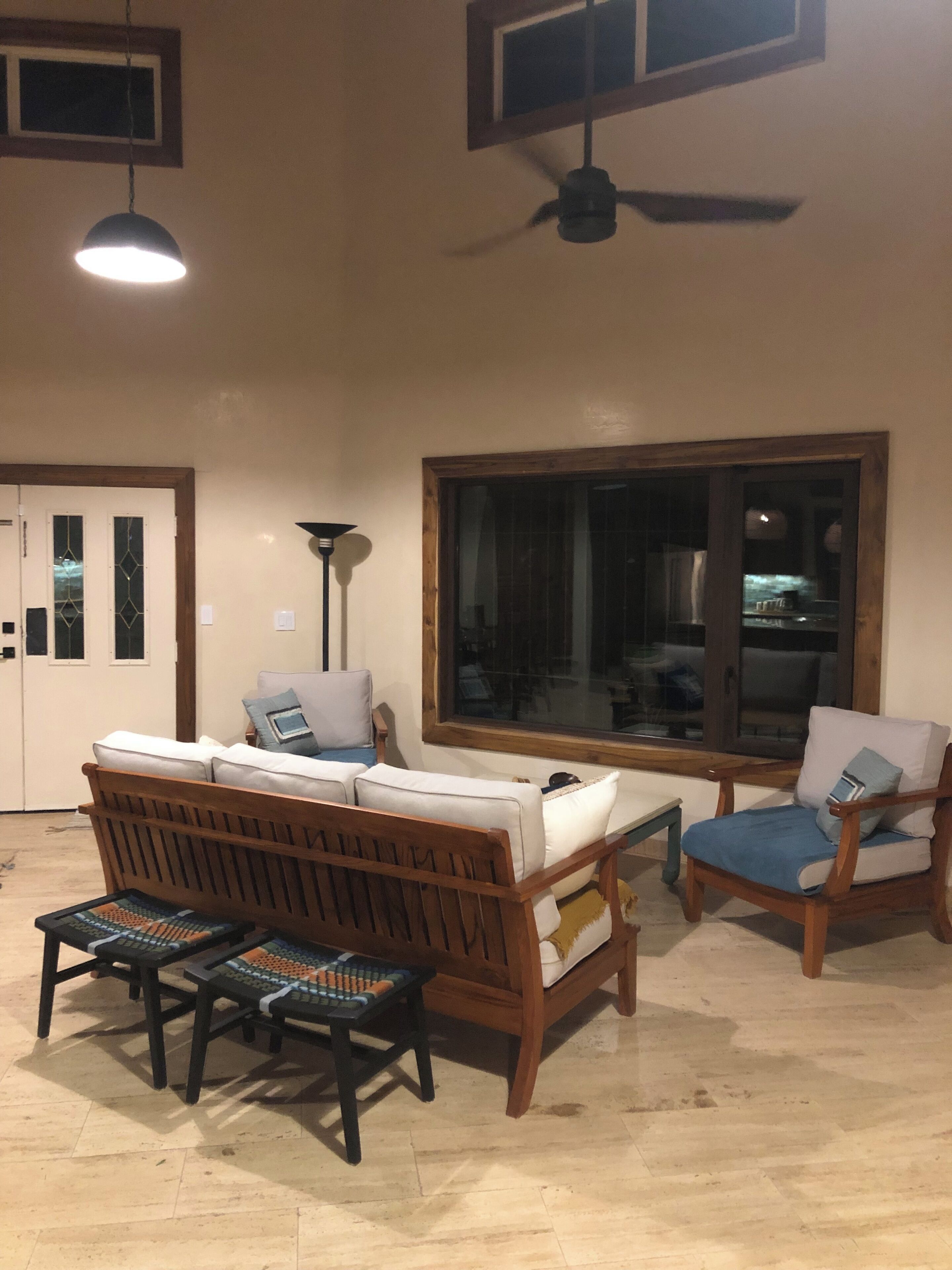 Un salon comprenant un canapé, deux fauteuils, une table basse et un lampadaire. Une grande fenêtre offre une vue sur l’extérieur.