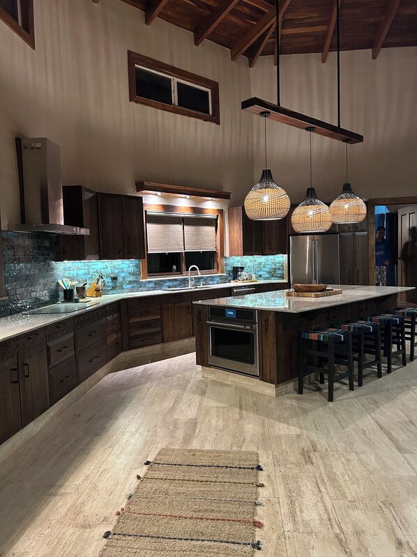 A modern kitchen with a large island, dark wooden cabinets, and a stone backsplash.
