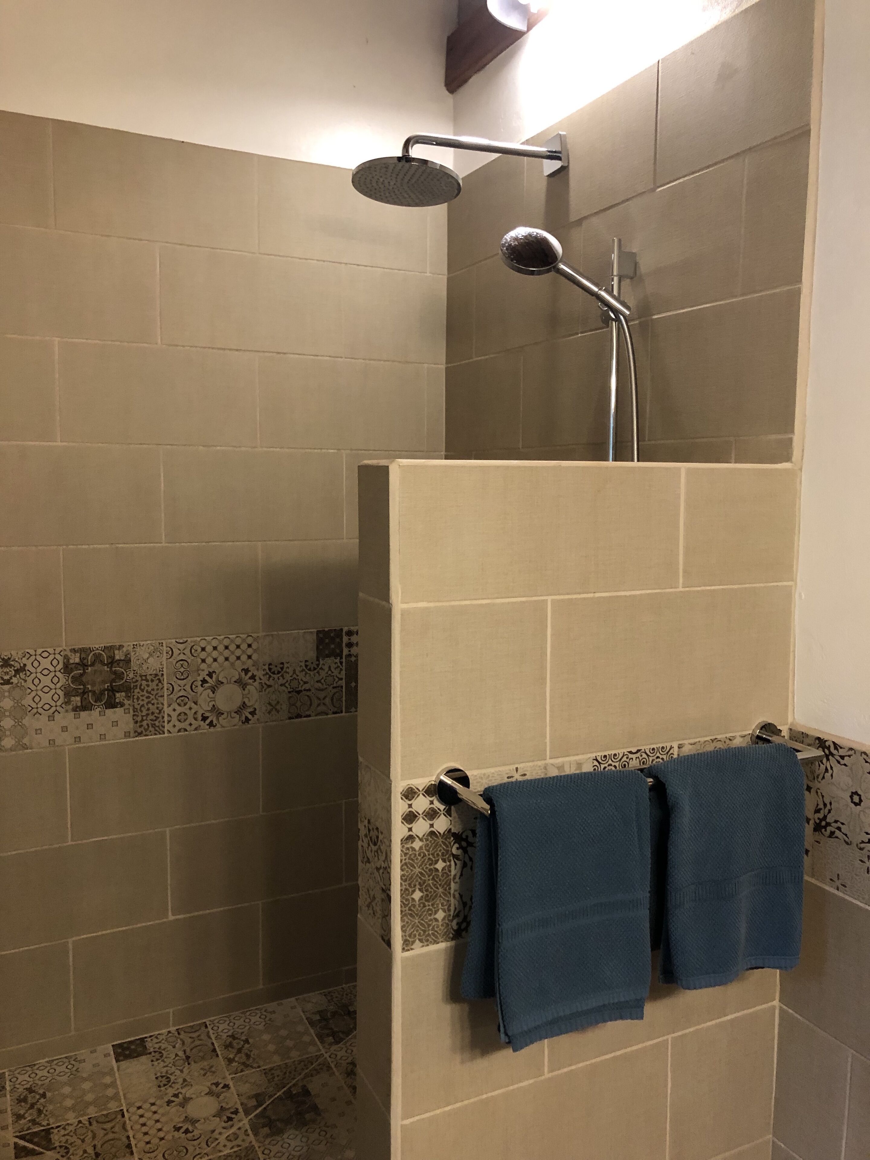 A shower with a handheld showerhead and a wall-mounted faucet. There are two towels hanging on a towel rack.