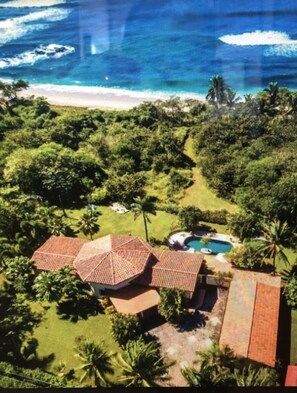 Vista aérea de um resort tropical com piscina, palmeiras e uma praia.