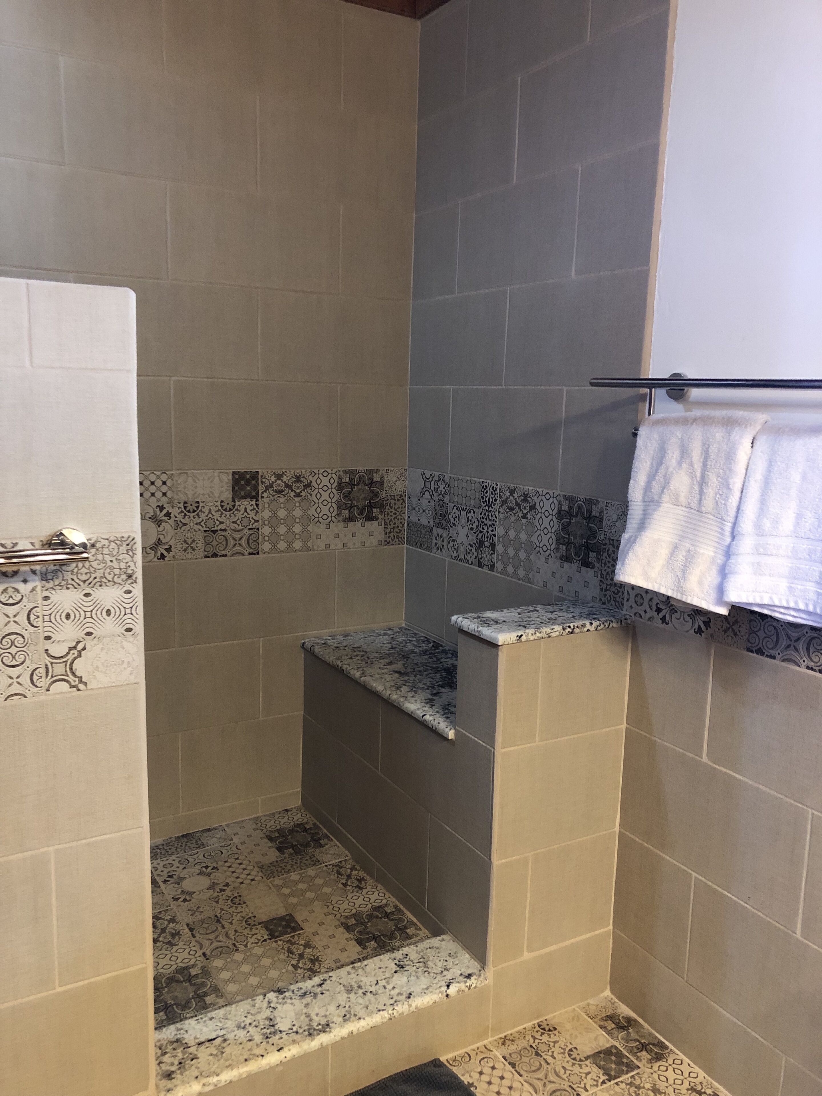 Un área de ducha con azulejos estampados, una encimera de mármol y un perchero.