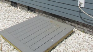 Une maison avec une fenêtre, un tuyau d’arrosage et une terrasse en bois.
