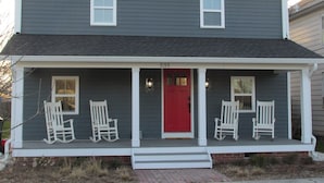 Une maison à deux étages avec une porte rouge, des fenêtres à cadre blanc et un porche agrémenté de fauteuils à bascule blancs.