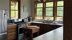 A kitchen with wooden cabinets, a stainless steel refrigerator, a stove, and a large window with a view of trees.