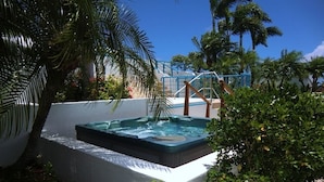 Un jacuzzi rodeado de vegetación exuberante y una palmera, con un cielo azul despejado al fondo.
