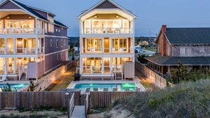 A two-story house with a balcony on the upper floor, a swimming pool in the backyard, and a wooden fence surrounding the property. - 5460- Virginia Dare, 8BR Oceanfront Retreat | Pool, Theater & Game Room (Nags Head)