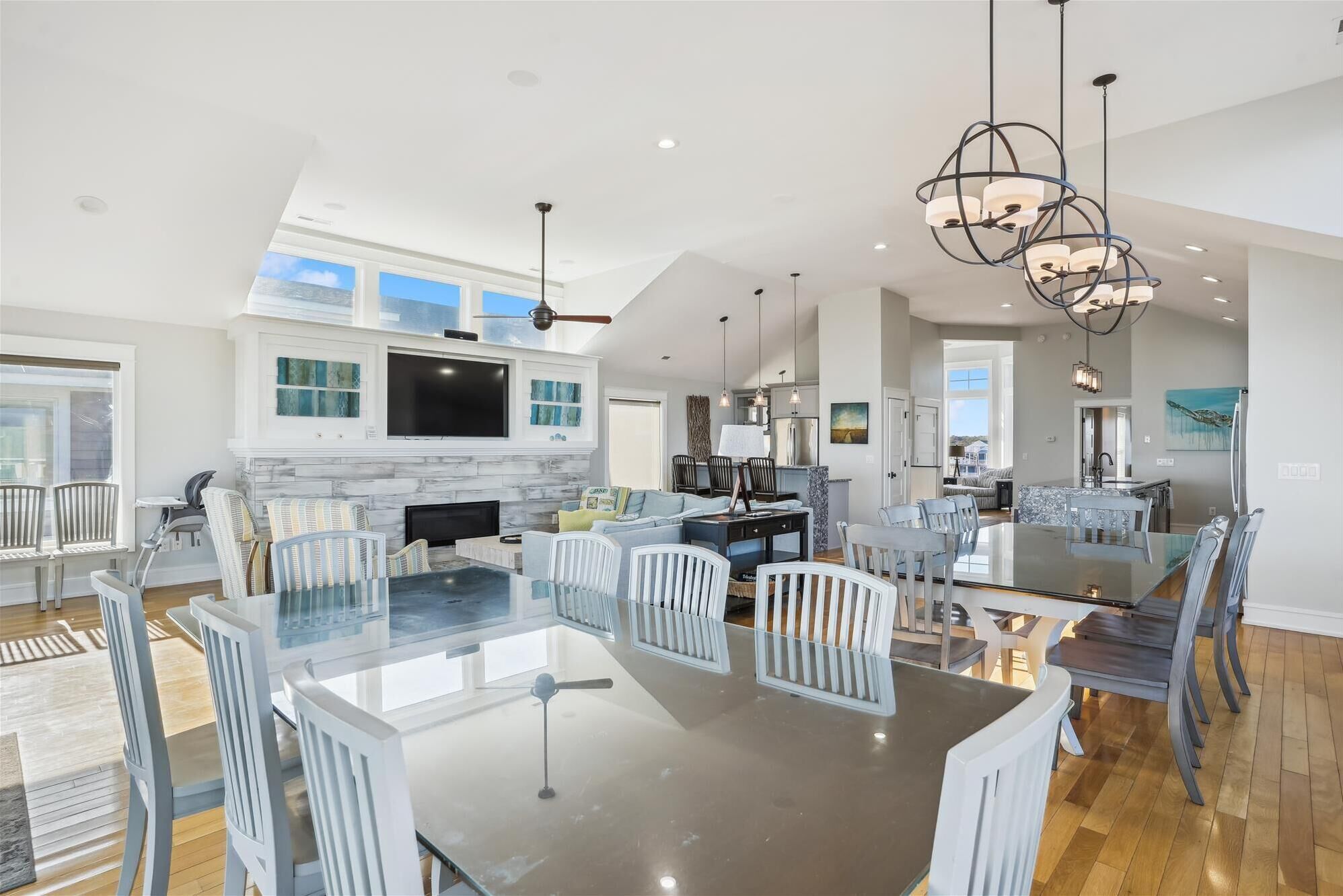 A spacious living area with a large glass-top dining table surrounded by white chairs, a fireplace, and a kitchen area with modern appliances.