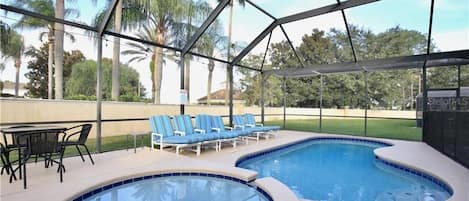 Una piscina interior con sillas reclinables azules y una mesa, rodeada por una estructura de techo metálico.