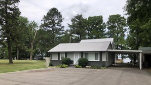 A single-story building with a covered porch, a small front yard, and a view of a body of water in the background.