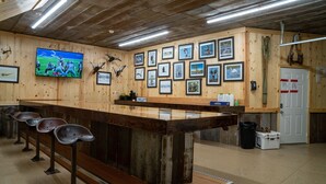 A bar area with wooden walls, framed pictures, and a television displaying a sports game.