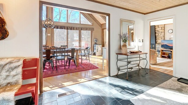 A spacious living area with a wooden ceiling, a dining area with a red rug, and a view of the outside.