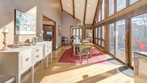 A spacious dining area with a large window, a chandelier, and a red rug.
