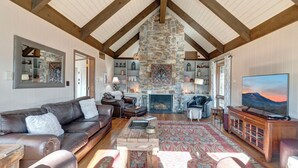 A spacious living room with a stone fireplace, wooden beams, a large TV, and a cozy seating area.