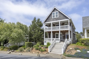 A two-story house with a porch, a staircase leading to the entrance, and a well-maintained garden with rocks and shrubs.
