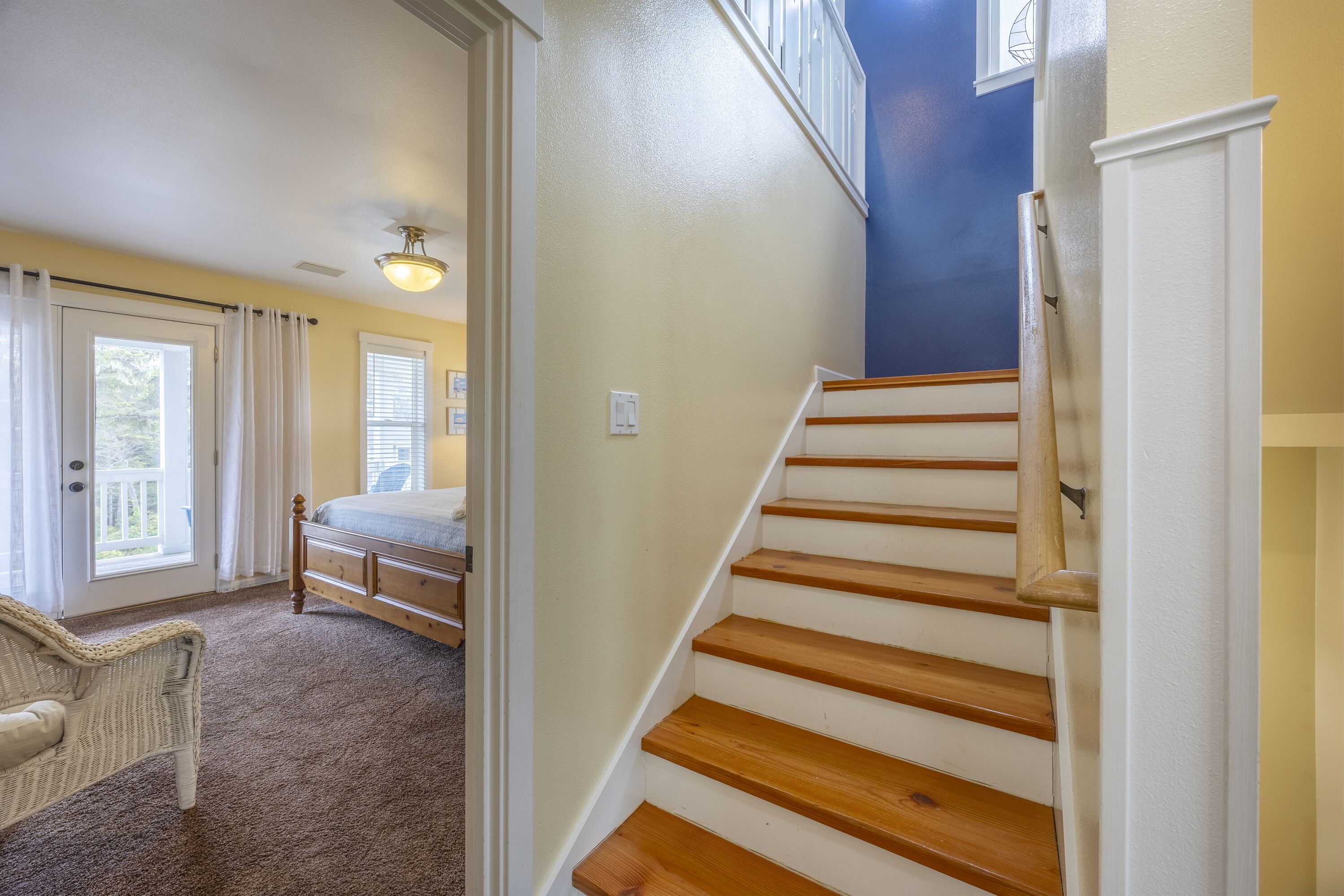 A bedroom with a bed, a chair, a staircase, and a door leading to another room.
