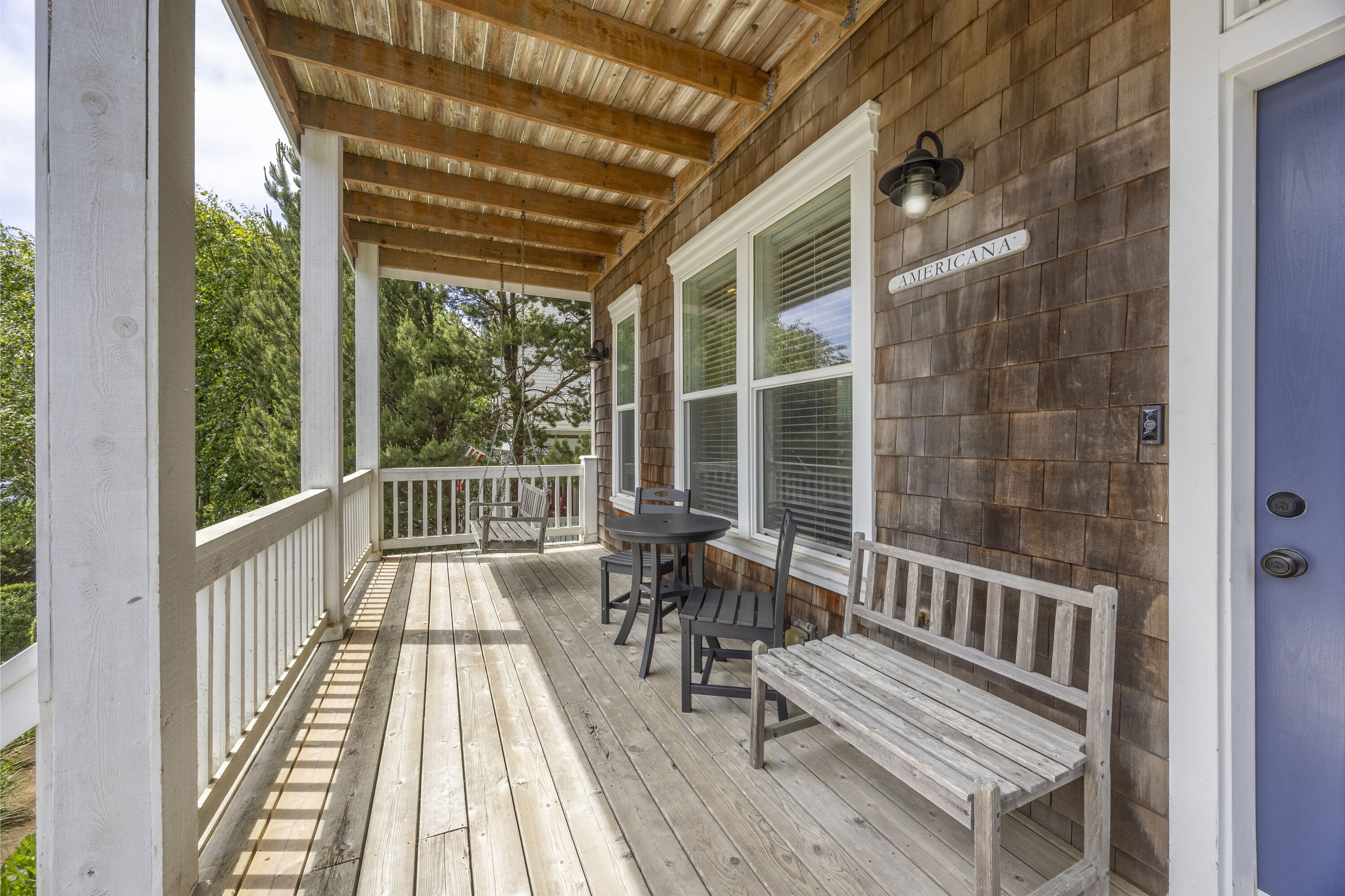 A wooden deck with white railings, a table with chairs, and a bench.