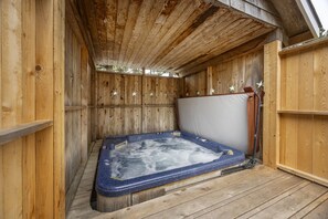 Un bain à remous en bois, doté d’un couvercle blanc, entouré de murs en bois et surmonté d’un plafond en pente.