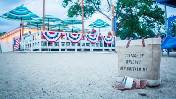 A beachside setting with umbrellas, a beach chair, and a tote bag with text. - Modern Farmhouse Just Steps From Town and Lake Michigan w/Heated Pool! (New Buffalo)