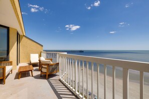 Enjoy the ocean view from this balcony with a table, two chairs, and a wicker seat.