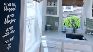 A compact kitchen with white cabinetry, a built-in dishwasher, and a window with a view of greenery outside.