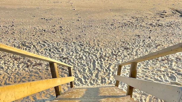A wooden staircase leading down to a sandy beach with a wooden railing on one side.