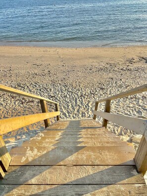 A wooden staircase leading down to a sandy beach with a wooden railing on one side. - Charming Cape Escape: Steps to the Beach, Large Deck, 2 Bikes & Outdoor Shower! (Dennis Port)