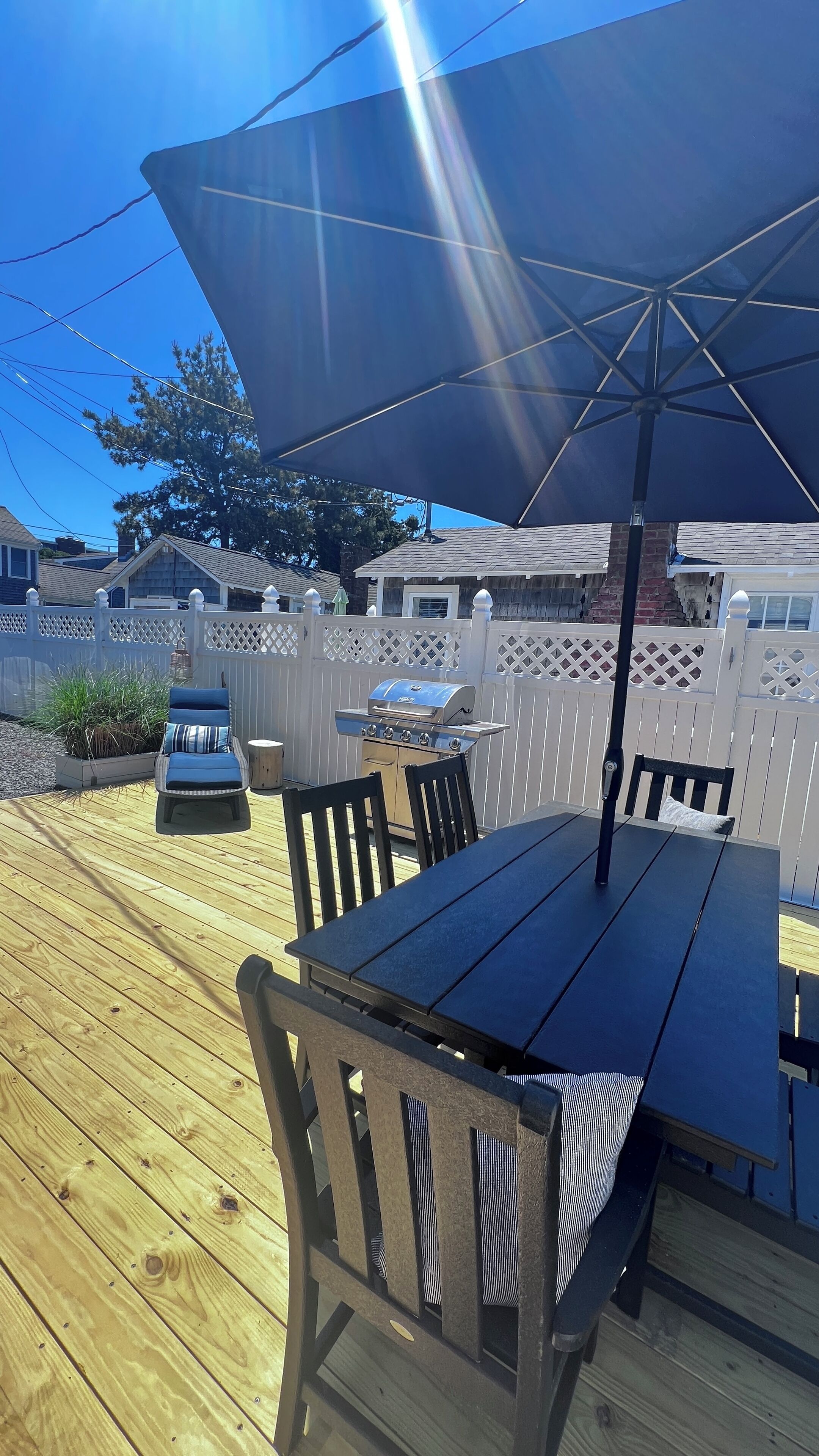 A wooden deck with a table and chairs, a grill, and a large umbrella.