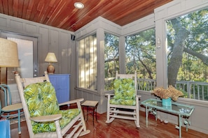 Relax in a serene setting with a comfortable seating area featuring a wooden ceiling, a small table, and two rocking chairs.