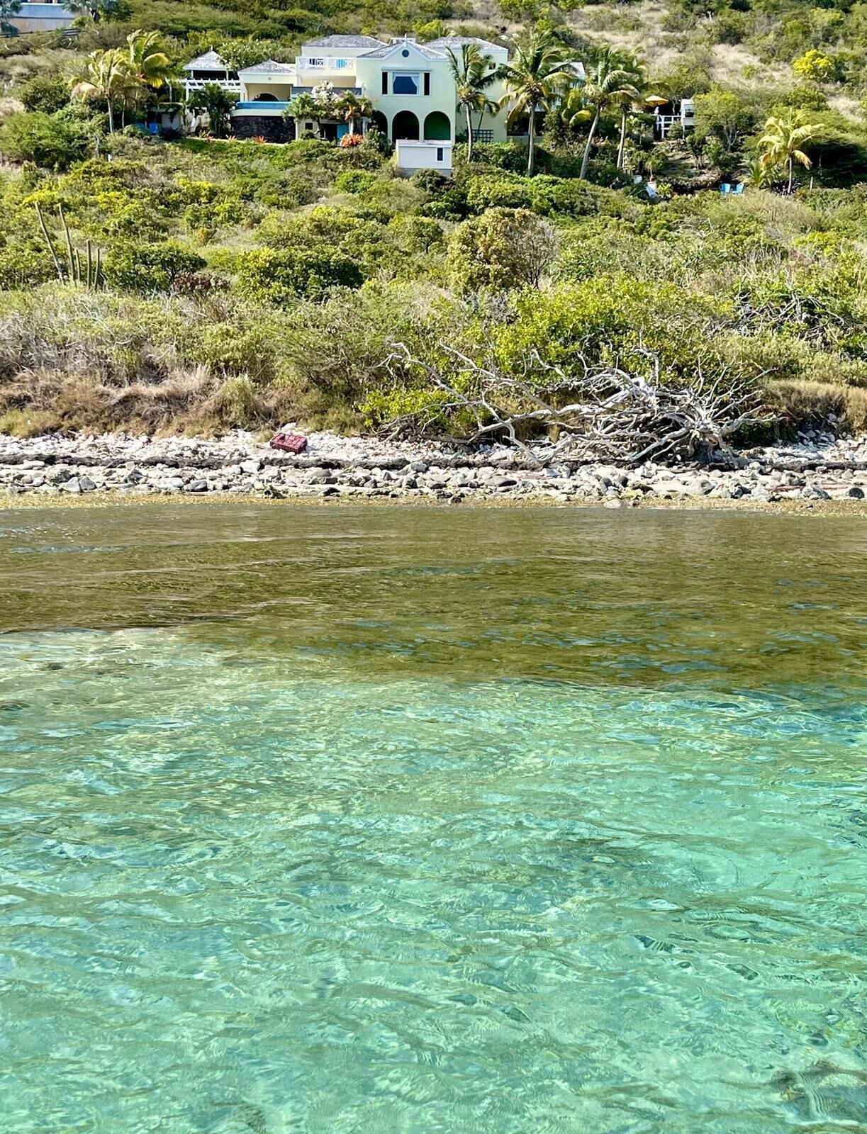 A coastal property with clear waters, a rocky shoreline, and a house surrounded by lush vegetation.