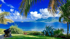 A lush green lawn with a stone structure, palm trees, and a view of the ocean and distant mountains. - St Kitts Two for One Luxury Villa & Private Lounge on beach breathtaking views! (South East Peninsula)