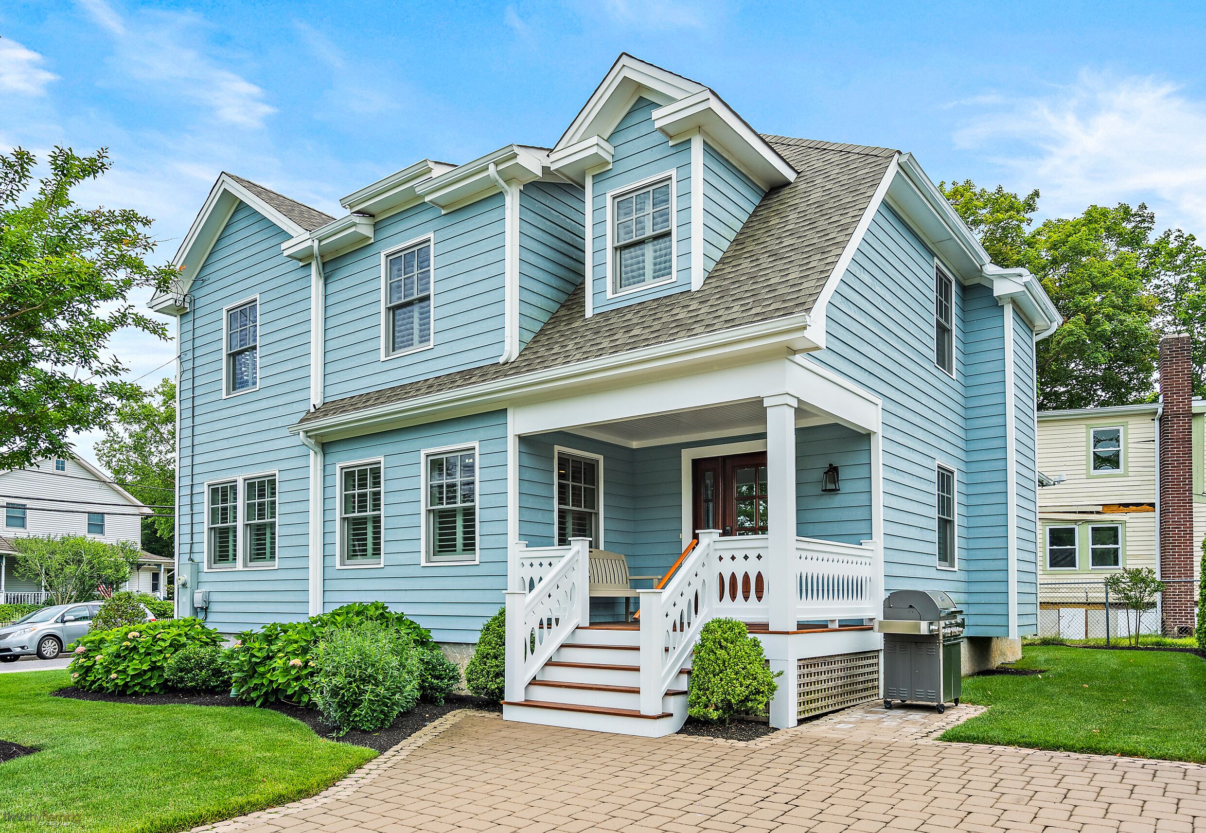 A two-story house with a porch, a staircase, and a grill in the yard.