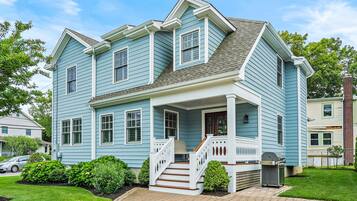 A two-story house with a porch, a staircase, and a grill in the yard.
