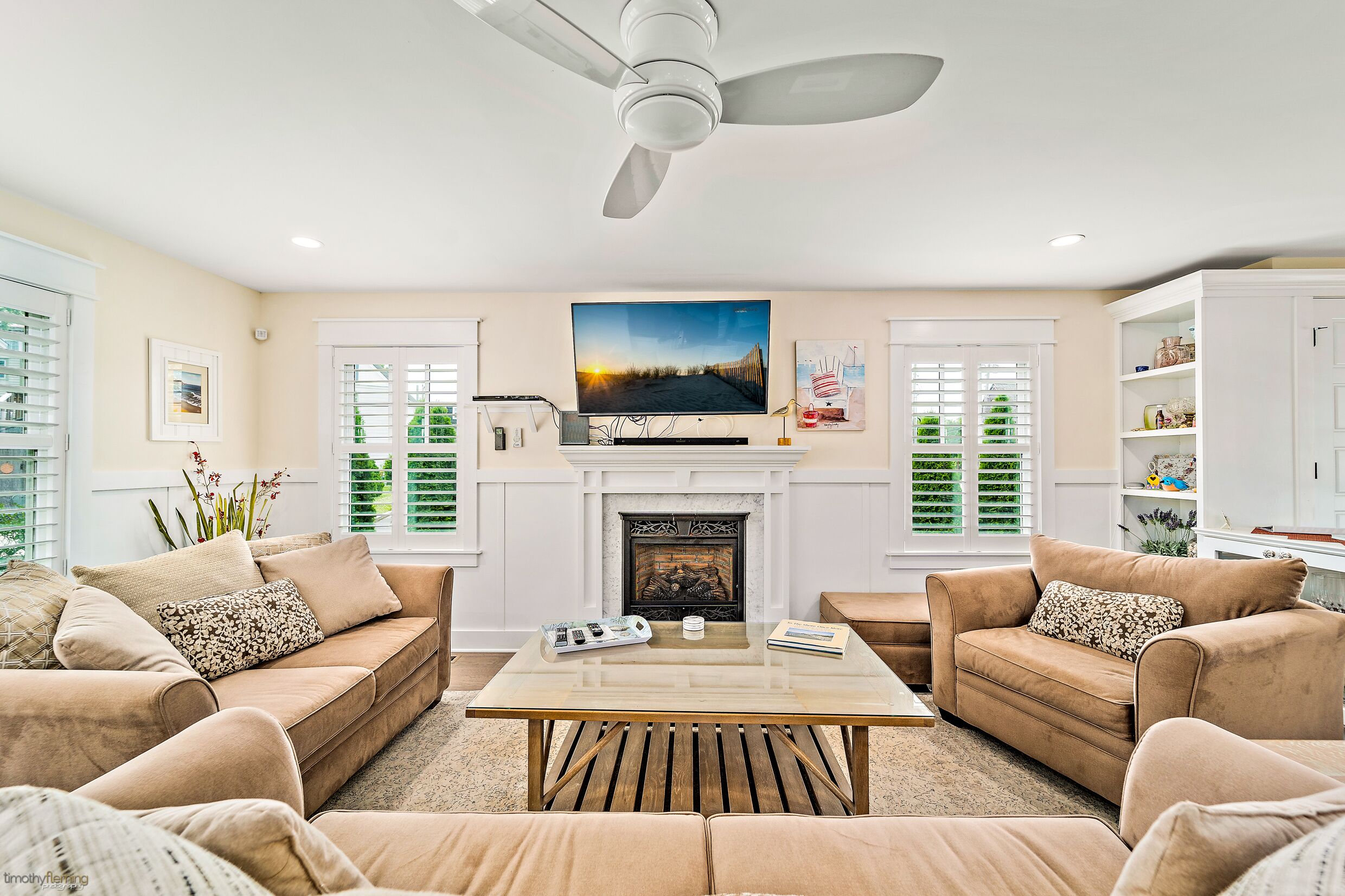 A living room with a fireplace, a ceiling fan, and a television mounted above it.