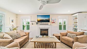 A living room with a fireplace, a ceiling fan, and a television mounted above it.