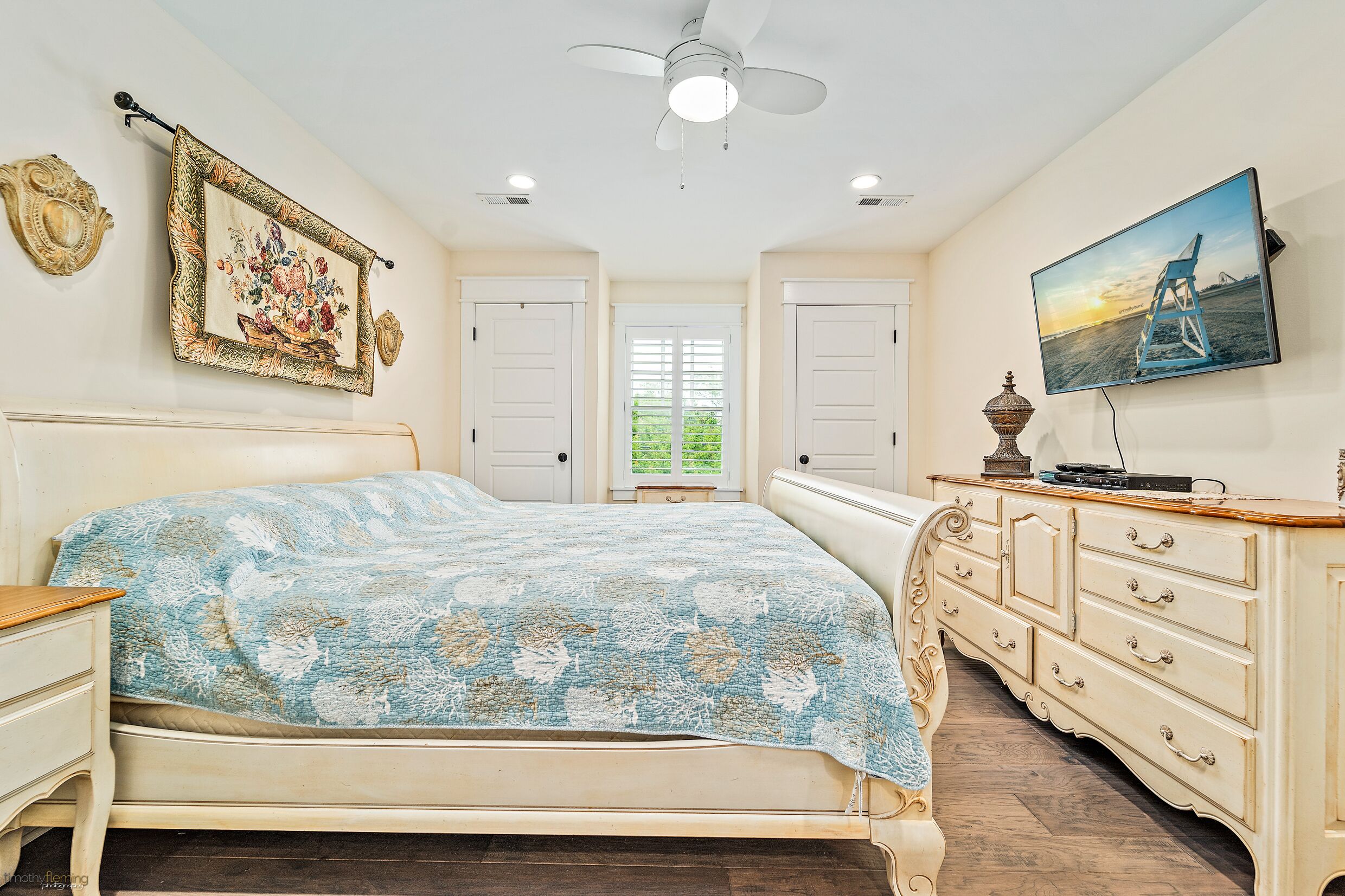 A bedroom with a bed, dresser, and a TV on the wall.
