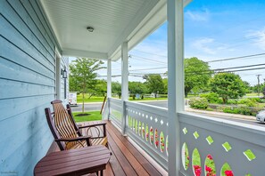 A porch with wooden chairs and a table, overlooking a street with a mailbox and a sign.