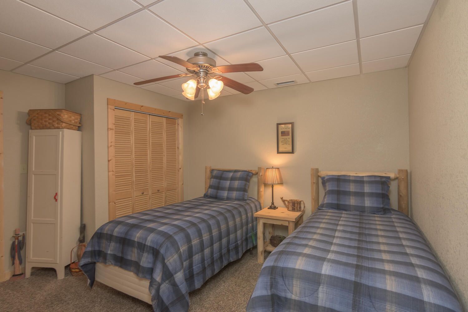A bedroom with two single beds, a ceiling fan, a wooden wardrobe, and a small bedside table with a lamp.