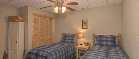 A bedroom with two single beds, a ceiling fan, a wooden wardrobe, and a small bedside table with a lamp.