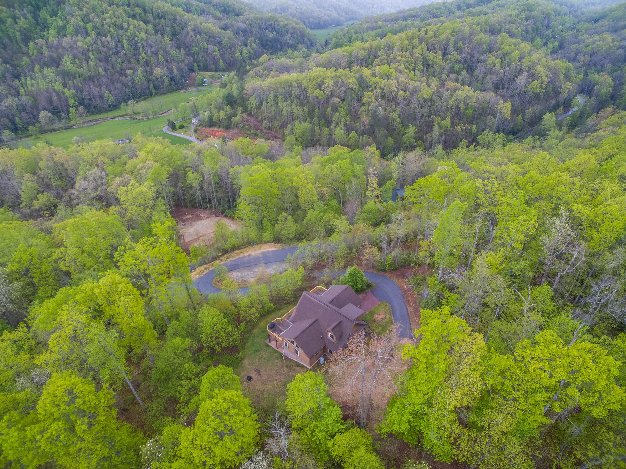 An aerial view of a house surrounded by dense forest, with a winding road leading to it.