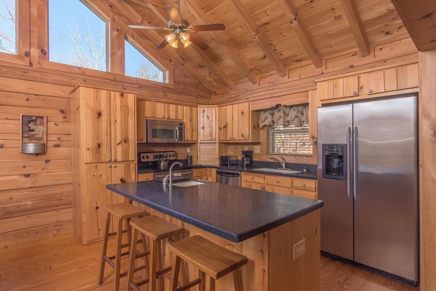 A wooden cabin-style kitchen with a central island, bar stools, a refrigerator, a microwave, and a stove.