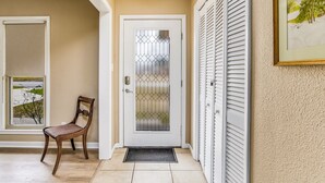 A hallway with a wooden chair, a white door with a glass panel, and a window with a view of a house and trees. - Near EVERYTHING House-Now Discounted for longer stays (Pensacola)