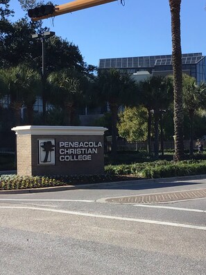 Señal de Pensacola Christian College con una palmera y un edificio al fondo.