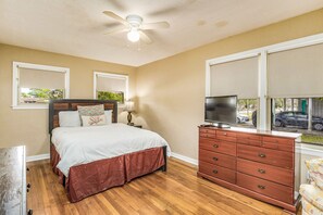 Un dormitorio con cama, cómoda, televisor y ventanas.