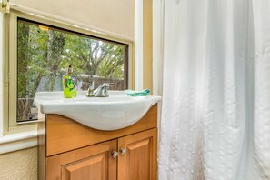 Un baño con lavamanos blanco, armarios de madera y ventana con vista a árboles.