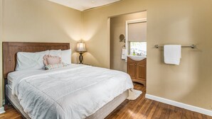 A bedroom with a bed, a nightstand, a lamp, a bathroom with a sink and mirror, and a ceiling fan. - Near EVERYTHING House-Now Discounted for longer stays (Pensacola)