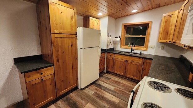 A compact kitchen with wooden cabinets, a white refrigerator, a sink, and a stove.