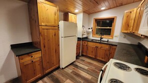 Una cucina compatta con mobili in legno, un frigorifero bianco, un lavello e un piano cottura.