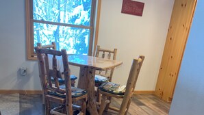 A dining area with a wooden table and chairs, a window with a view of trees, and a sign on the wall.