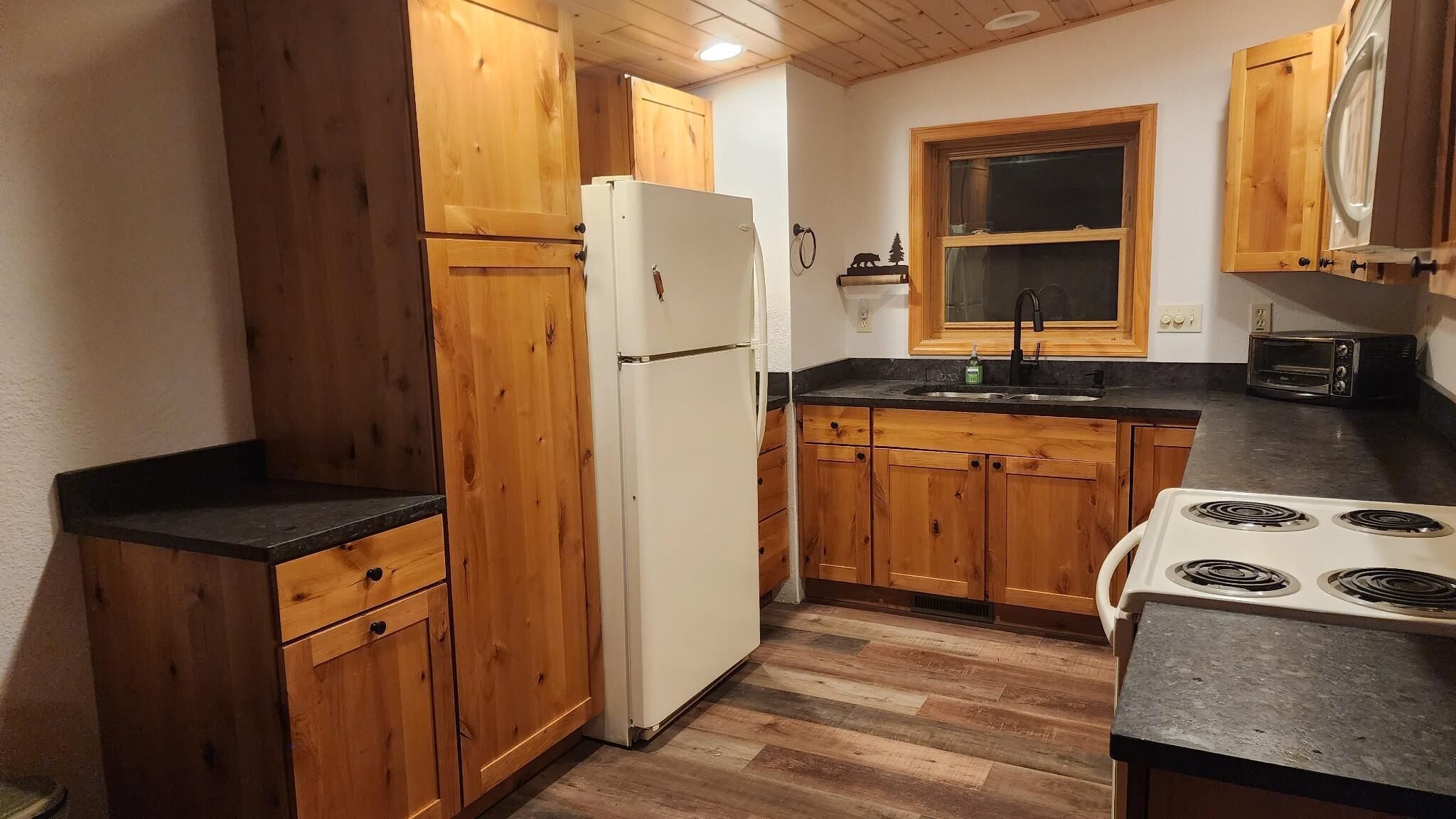 A compact kitchen with wooden cabinets, a white refrigerator, a sink, a stove, and a toaster oven.