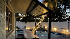 A covered outdoor area with a pool, wooden benches, and string lights. - Anna Maria 2 Family Home w/ pool, beach/3 blocks. (Holmes Beach)
